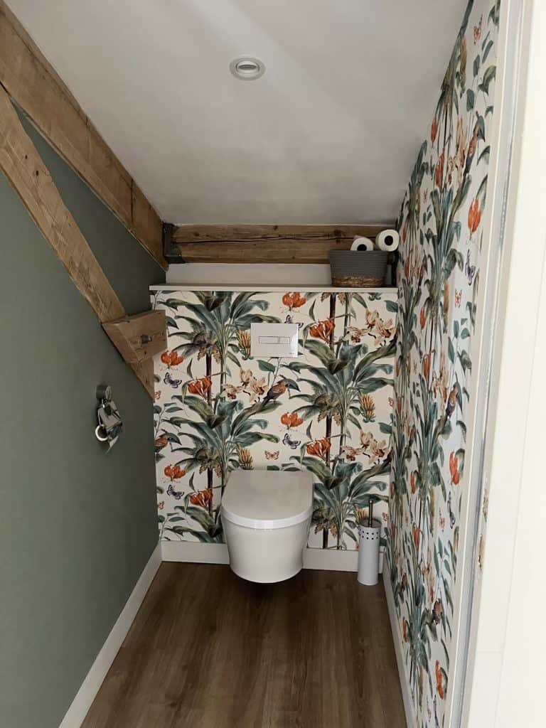 Toilettes design avec papier toilette sur étagère et décoration florale tropicale.