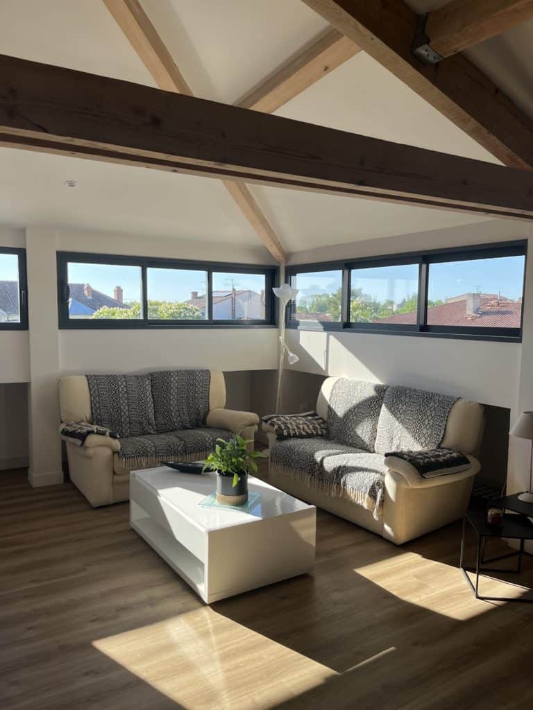 Luminaire dans un salon moderne aux poutres en bois, luminosité naturelle optimale, espace confortable.