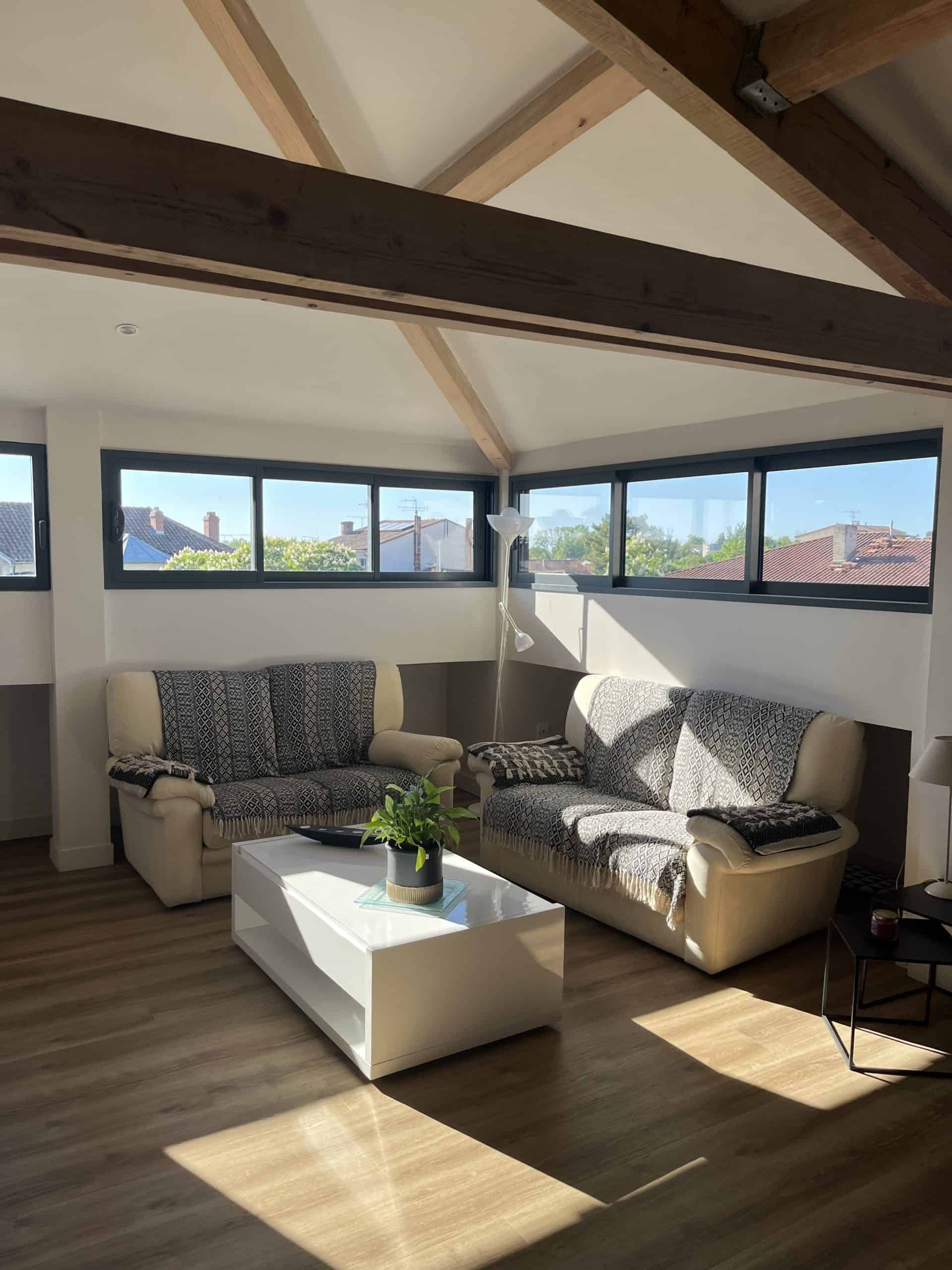 Luminaire dans un salon moderne aux poutres en bois, luminosité naturelle optimale, espace confortable.