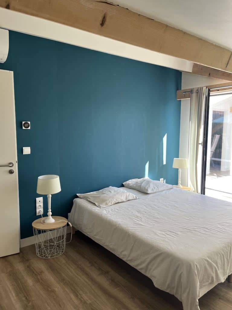 Lit avec mur bleu, chambre chaleureuse avec luminaires et terrasse ensoleillée.